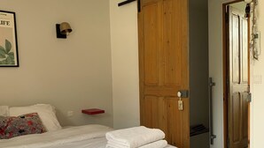 A bedroom with a bed, a wooden wardrobe, a door, and a wall-mounted light fixture.