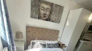Un dormitorio con cabecera capitonada, cama con almohadas estampadas, mesita de noche con lámpara y una obra de arte grande sobre la cama.