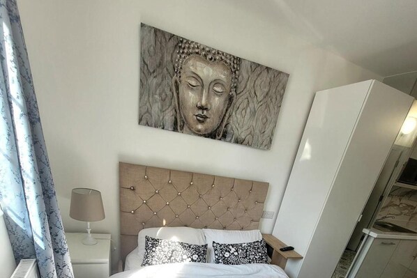A bedroom with a tufted headboard, a bed with patterned pillows, a nightstand with a lamp, and a large artwork above the bed.