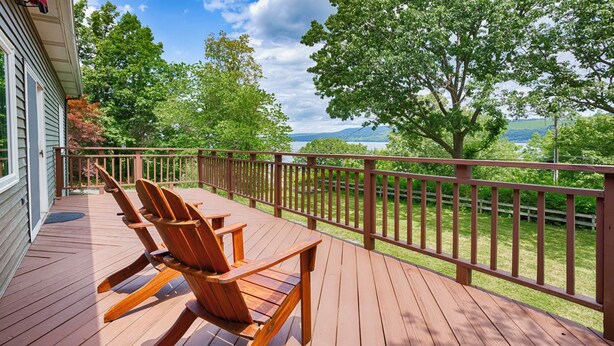 Terraza de madera con sillas Adirondack y vista a un lago y montañas.