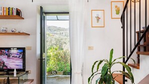 Ένα σαλόνι με τηλεόραση, βιβλία και ένα φυτό. Υπάρχει μια σκάλα και μια πόρτα που οδηγεί έξω.