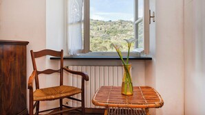 Ένα δωμάτιο με μια ξύλινη καρέκλα, ένα τραπέζι από μπαμπού και ένα παράθυρο με θέα σε έναν λόφο.