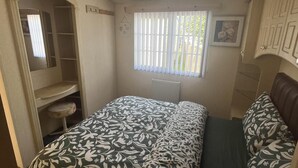 Ein kleines Schlafzimmer mit Bett, einem kleinen Hocker, einem Fenster mit Jalousien und einer Heizung.