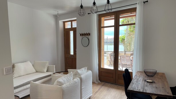 Una sala de estar moderna con un conjunto de sofá, una mesa de comedor con sillas y vistas al mar a través de grandes ventanales.
