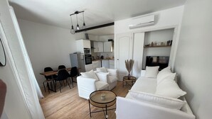 Una sala de estar moderna con un sofá blanco, un comedor con una mesa y sillas de madera, y una cocina al fondo.