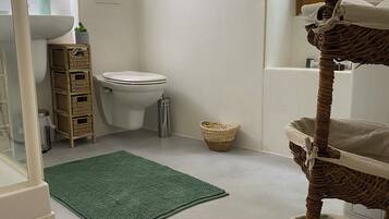 A bathroom with a toilet, a green rug, wicker baskets, and a window.