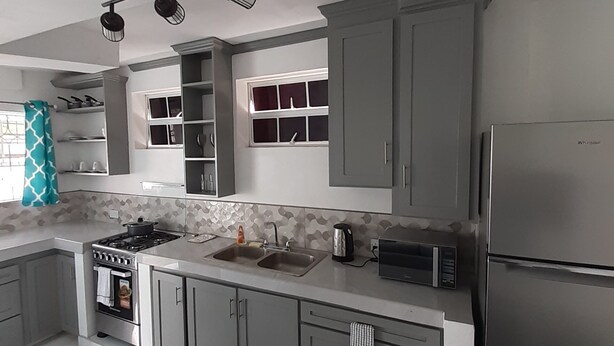 A modern kitchen with grey cabinets, a stainless steel refrigerator, a microwave, a stove, and a sink. - Luxury Retreat Between City & Rodneybay-free Treat (Castries)