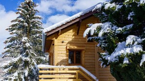 Une cabane en bois avec un escalier en bois menant à un porche, le tout entouré d’arbres couverts de neige.