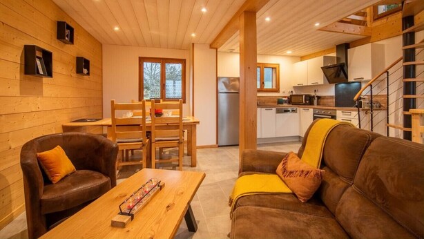 Un intérieur chaleureux avec un coin repas en bois, un canapé et une cuisine équipée d’appareils électroménagers modernes.