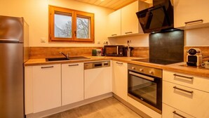 Une cuisine moderne avec des meubles blancs, un four encastré, un four à micro-ondes et une fenêtre donnant sur les arbres.