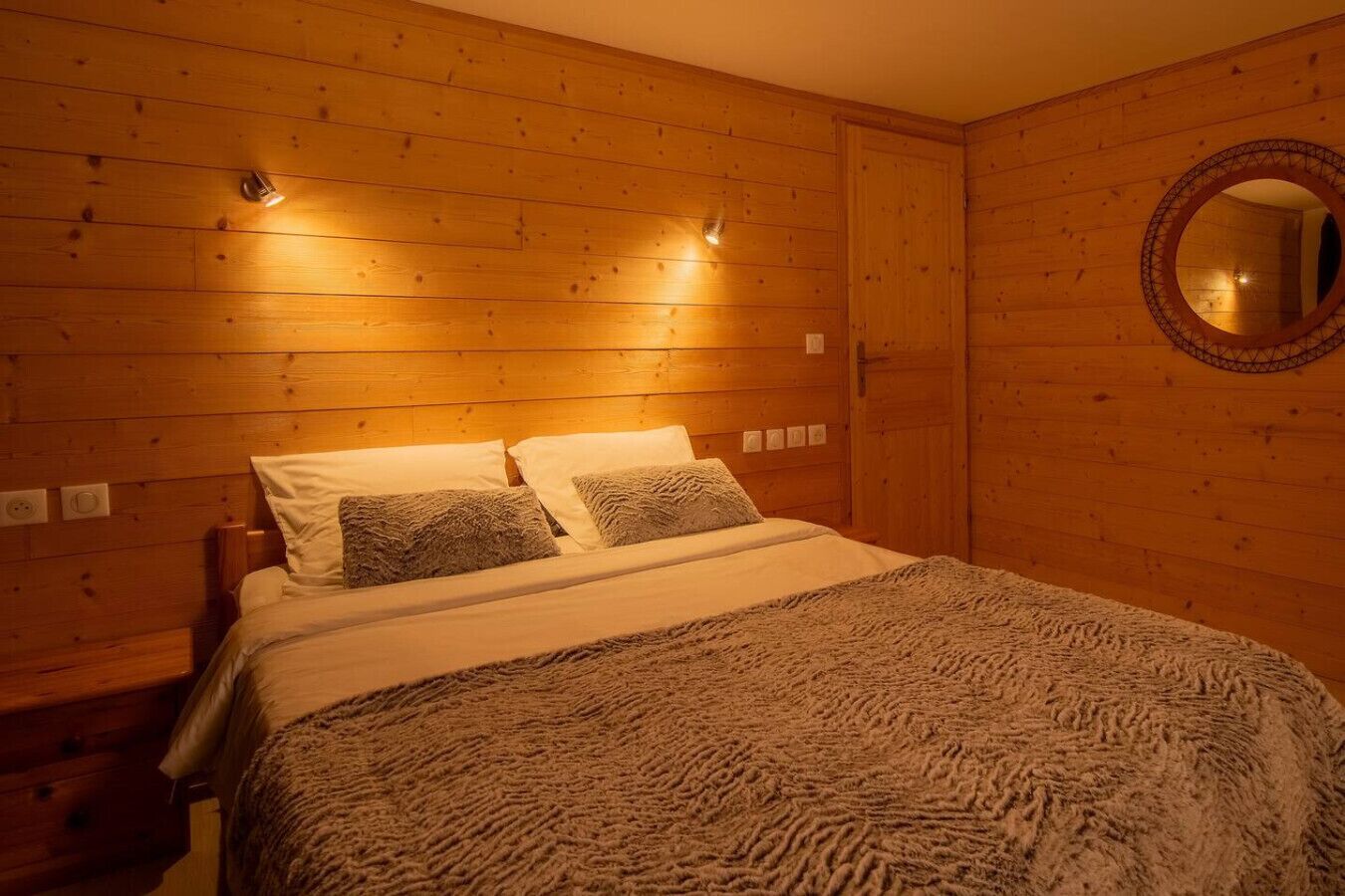 Ein Zimmer mit Holzwänden, einem Bett, zwei Wandleuchten, einem runden Spiegel und einer Steckdose.