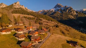 A cluster of wooden houses with sloped roofs, surrounded by a mountainous landscape and a clear sky. - Chalet Altitude - Panoramic view - 8 pers (Bernex)