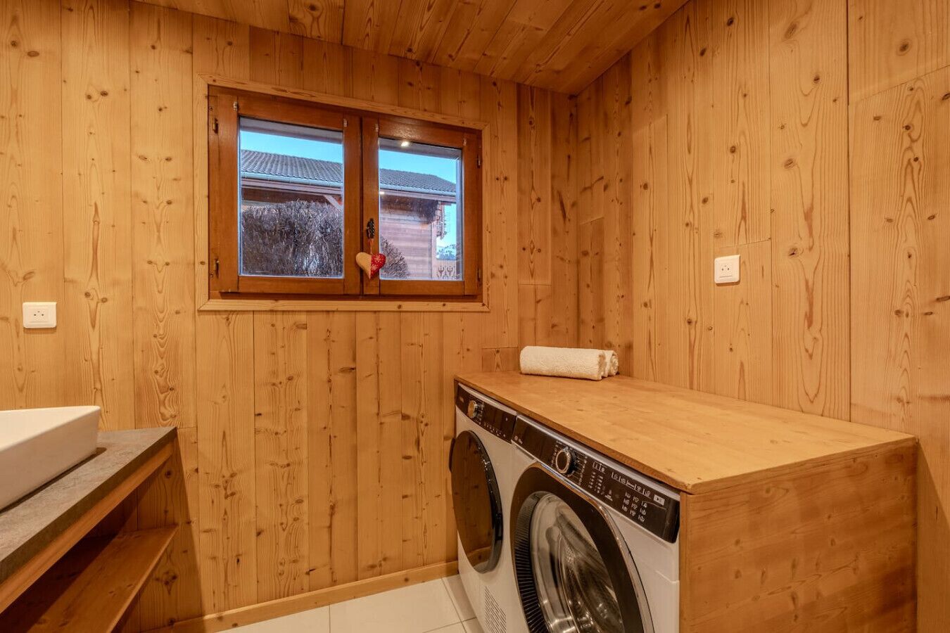 A wooden-walled laundry room with a washing machine, a sink, and a window.