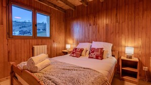 A wooden-paneled bedroom with a bed, two bedside lamps, and a window with a view of a landscape. - Chalet Altitude - Panoramic view - 8 pers (Bernex)
