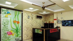 A reception area with a tiled floor, a ceiling fan, a clock, and a television mounted on the wall. - Hotel Chetali (Bijnor)