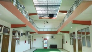 A spacious indoor area with a green carpet, a Coca-Cola refrigerator, and a television on the wall. - Hotel Chetali (Bijnor)