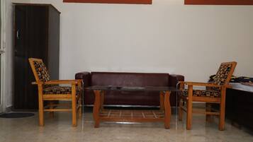 Una habitación con un sofá de cuero marrón, dos sillas de madera con cojines estampados y una mesa de centro de vidrio.