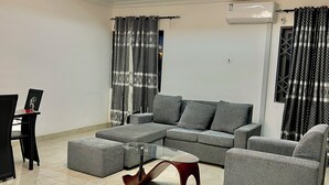 A modern living room with a sectional sofa, a glass coffee table, and a ceiling fan. - ES Homes-2Bedroom Apartment at Achimota (Accra)