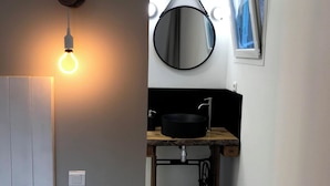 A narrow hallway with a round mirror, a round light fixture, and a sink with a black basin.