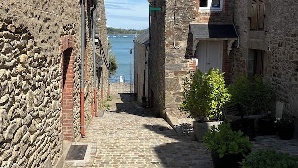Uma rua de paralelepípedos estreita, ladeada por edifícios de pedra, com vista para o mar.