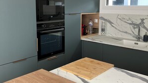 Cozinha moderna com armários escuros, forno embutido, mesa de madeira e painel de fundo de mármore.