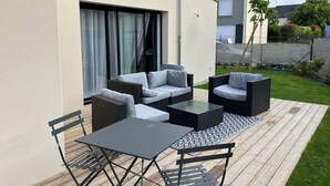 Um pátio externo com mesa e cadeiras, um conjunto de sofás e vista para uma casa ao fundo.