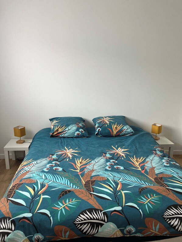 Una cama con colcha y almohadas estampadas, flanqueada por dos mesitas de noche con lámparas.