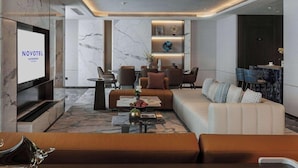Een moderne hotellobby met een bank, stoelen, een salontafel, een televisiescherm en een receptiebalie.