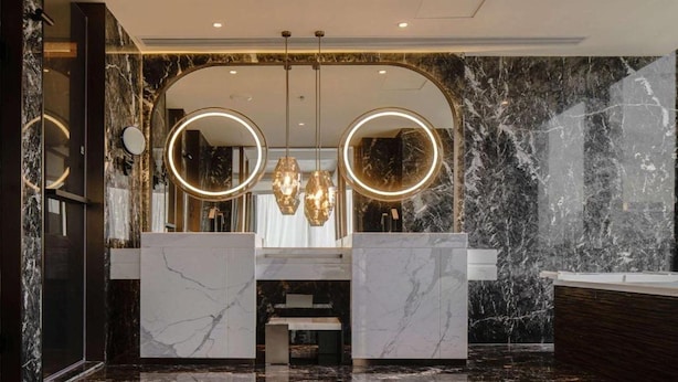 Een moderne badkamer met marmeren wanden, twee wastafels en een kroonluchter.