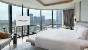 Een moderne hotelkamer met een groot bed, een bank, een kleine tafel en uitzicht op de stad door grote ramen.