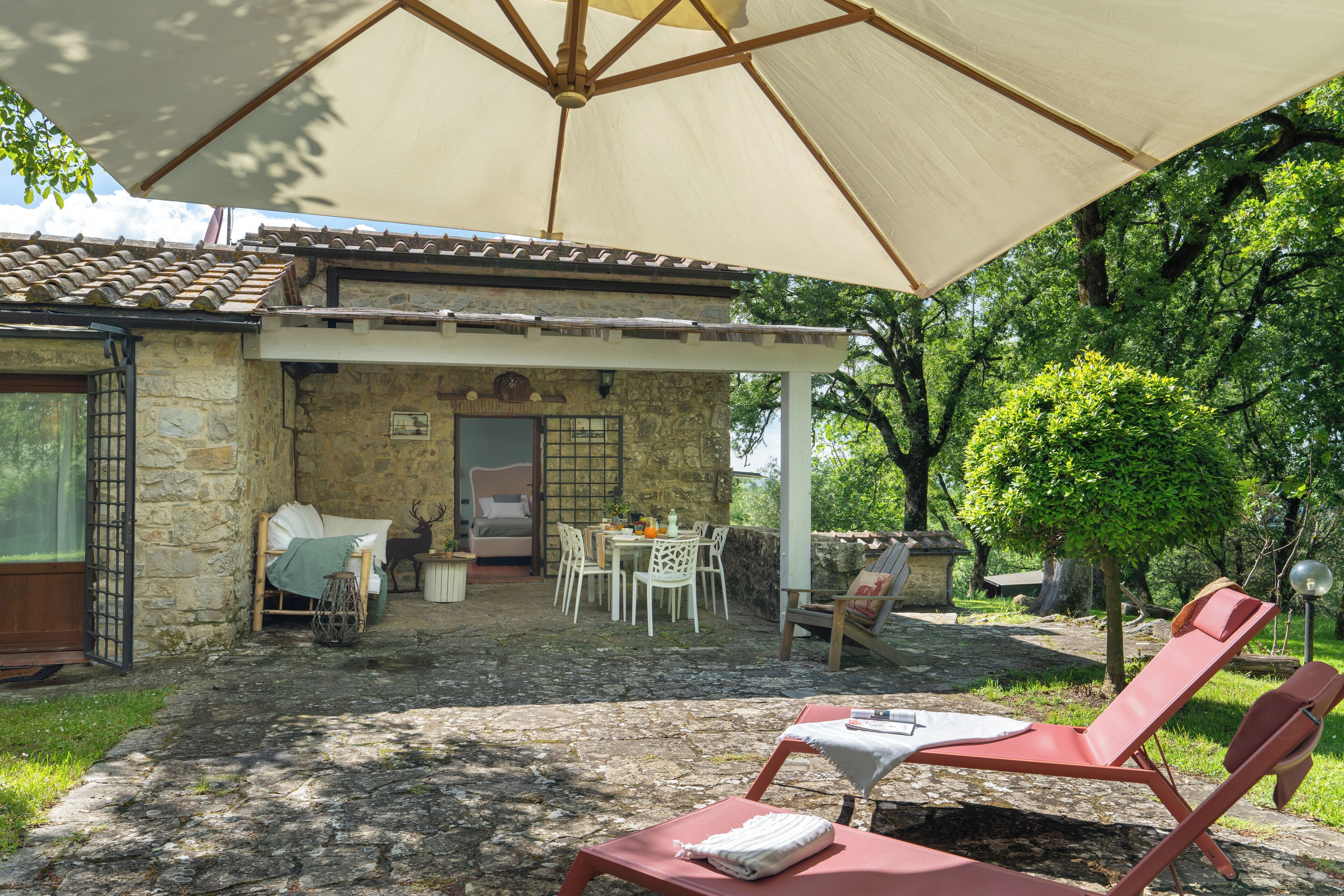 A stone building with a tiled roof, a covered patio with a table and chairs, and two red lounge chairs.