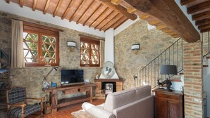 A rustic living room with a stone wall, wooden beams, a fireplace, a sofa, a television, and a wooden bench. - A Casa Dell'ida (Castellina in Chianti)