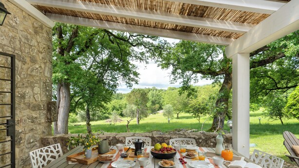 An outdoor dining area with a stone wall, white chairs, and a table set for breakfast. - A Casa Dell'ida (Castellina in Chianti)