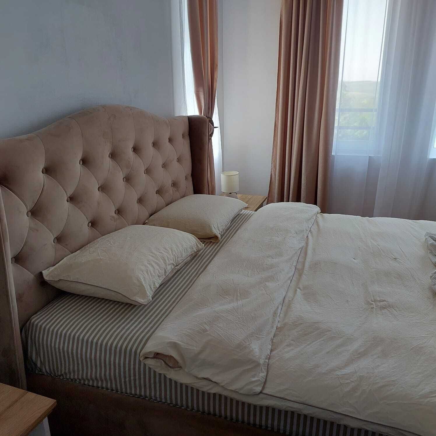 A bedroom with a tufted headboard, a bed with striped bedding, and a bedside table with a lamp.