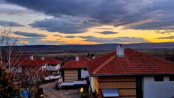A rural village with traditional red-tiled roofs and white walls, surrounded by open fields and hills.