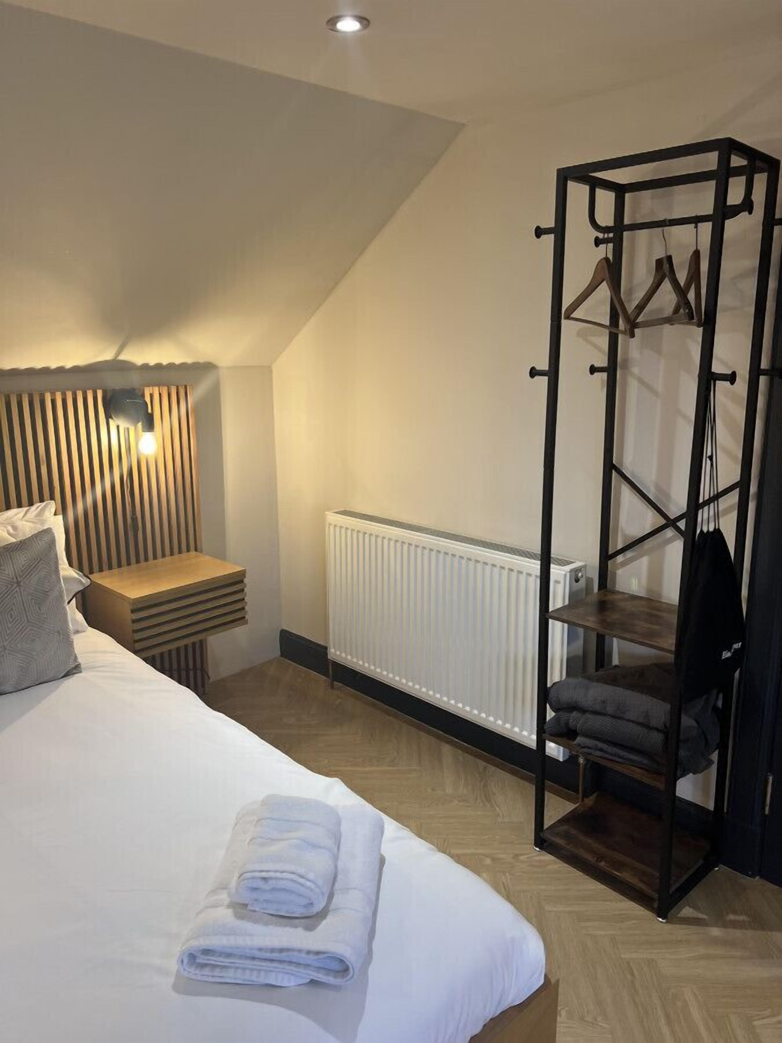 Ein Schlafzimmer mit Bett, Nachttisch, Heizkörper und einer Kleiderstange.