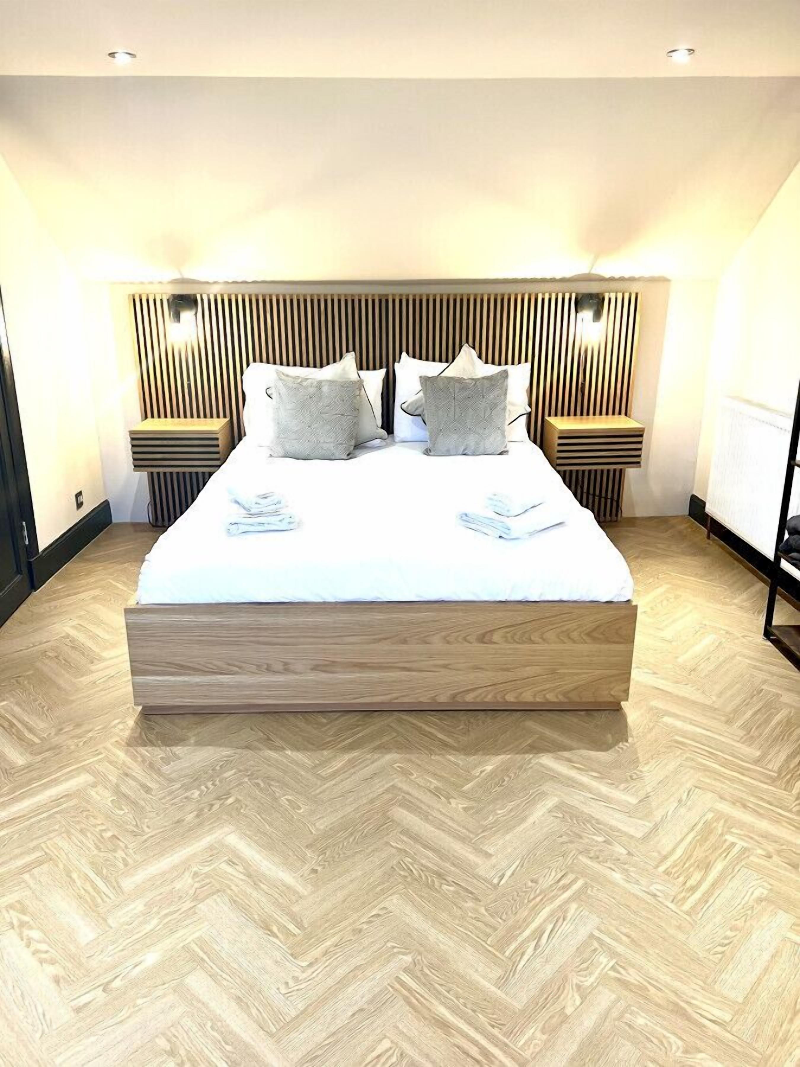 Ein modernes Hotelzimmer mit einem großen Bett, einem Holz-Kopfende und einem Fischgrätparkett.
