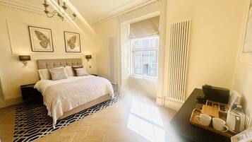 A hotel room with a large bed, a bedside table with a tray of breakfast items, a radiator, and a window with curtains.