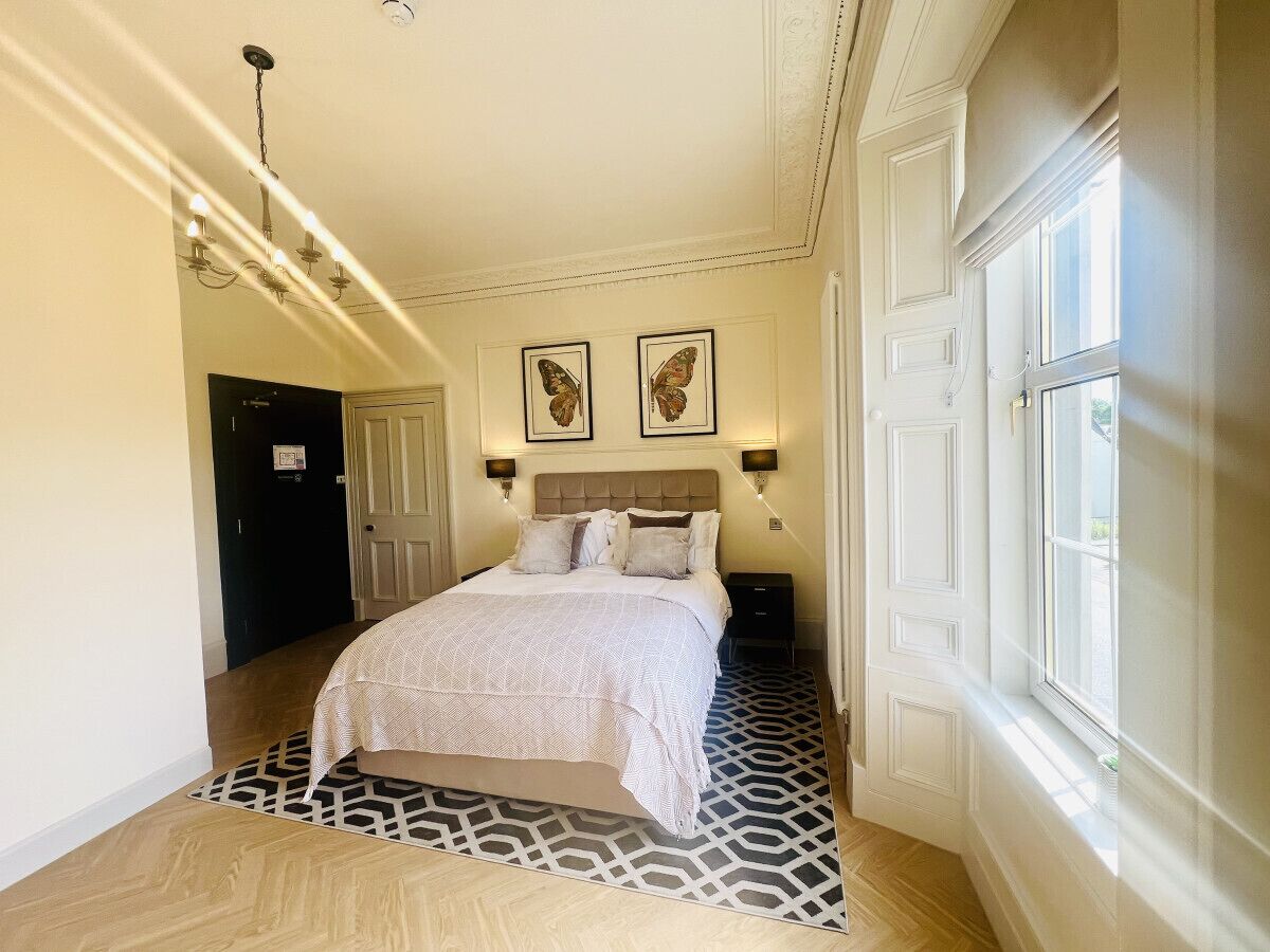 A bedroom with a bed, a patterned rug, a chandelier, and two wall-mounted lamps.