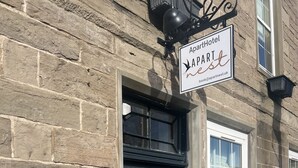 A stone building with a dark grey door, a sign reading 'ApartHotel Apartnest,' and a small potted plant beside the door. - 'Mac' in ApartNest ApartHotel (Auchterarder)
