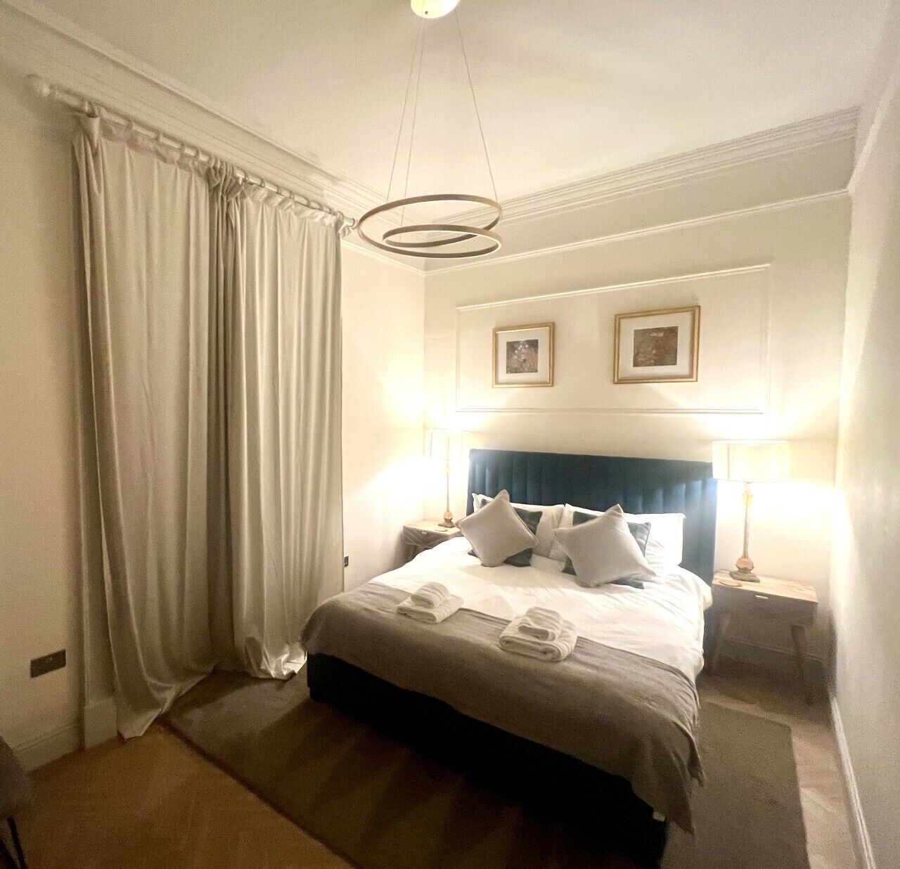 A hotel room with a large bed, two bedside tables, a ceiling light fixture, and a window with curtains.