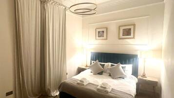 A hotel room with a large bed, two bedside tables, a ceiling light fixture, and a window with curtains.