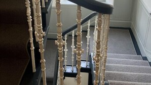 En trappa med utsmyckade trappspjälor och ett svart handledare, som leder upp till en liten plattform med utsikt över en byggnad utanför.