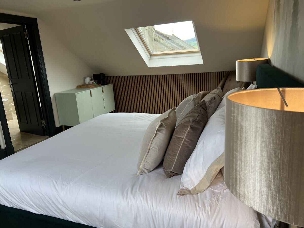 Ein Schlafzimmer mit Dachfenster, einem Bett mit Kissen, einem Nachttisch und einer Lampe.