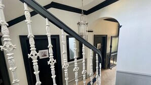 A staircase with ornate white balusters and a black handrail, leading to a landing with a chandelier.