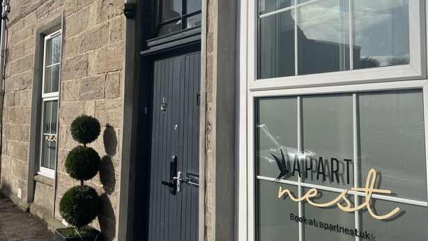 A building with a sign reading "ApartHotel APART nest" and a large window with the same branding.