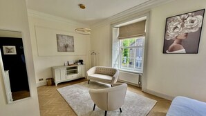 A spacious room with a large window, a white sofa, a white armchair, and a white cabinet.