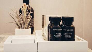 Un meuble-vasque de salle de bain sur lequel repose un plateau blanc contenant deux bouteilles étiquetées « GROWN ALCHEMIST » et une boîte blanche.