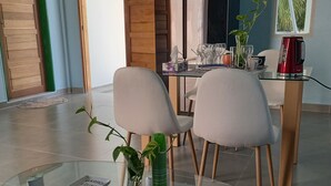 A modern dining area with a glass table, two white chairs, a red kettle, and a wooden cabinet. - IRUKA GUESTHOUSE (Fiyoaree)