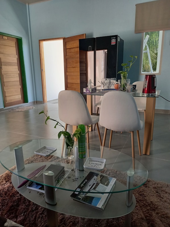 A modern dining area with a glass table, two white chairs, a red kettle, and a wooden cabinet.